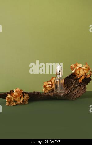 Flasche mit ätherischem Öl, Holz und Blumen auf grünem Hintergrund. Hausgemachtes Mittel- und Beauty-Produktkonzept. Stockfoto