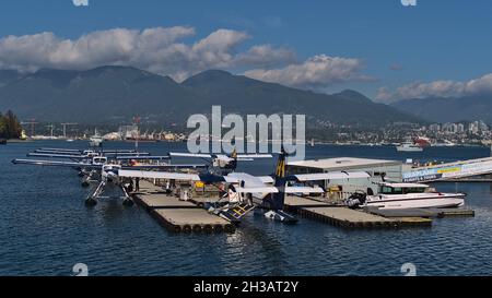 Blick auf aufgereihte Wasserflugzeuge, die von der Fluggesellschaft Harbour Air im Vancouver Harbour Flight Centre mit Bergen im Hintergrund betrieben werden. Stockfoto