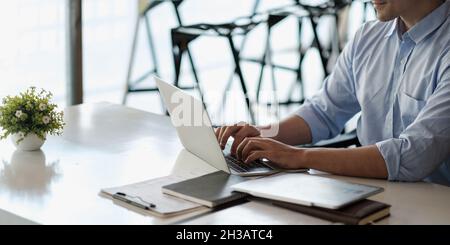 Lächelnder Geschäftsmann, der im Büro einen Laptop benutzt. Männliche Hände tippen auf der Notebook-Tastatur.Konzept der jungen Menschen arbeiten mobile Geräte Stockfoto