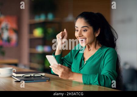 Emotionale Dame aus dem Nahen Osten, die gute Nachrichten hat und Handy benutzt Stockfoto