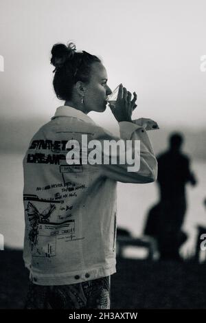 SEVAN, ARMENIEN - 03. Sep 2021: Eine monochrome Aufnahme einer Frau, die auf einer Strandparty in der Nähe des Sevan-Sees ein armenisches Bier genießt Stockfoto