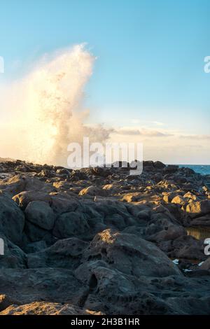 Meereswellen plätschern in der Nähe der felsigen Küste gegen den wolkigen blauen Himmel bei Sonnenuntergang Stockfoto