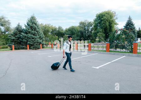 Ein junger gutaussehender Mann arabischen Geschäftsmann Unternehmer Tourist Traveler Besucher gehen mit Koffer für Trip in seiner Hand in Parkplatz . Stockfoto