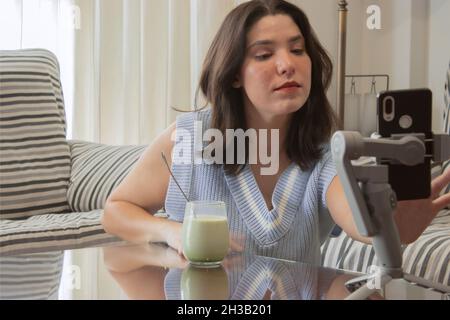 Eine junge Bloggerin, die mit ihren Followern ein Live-Video für ihre sozialen Medien abhält und gleichzeitig ihren Lieblingsmatcha Latte hält. Wellness-Konzept. Stockfoto