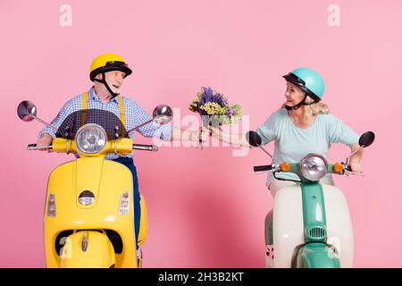 Foto von glücklichen reifen Ehepaar im Helm Mann geben Frau Strauß Fahrt Moped isoliert auf rosa Hintergrund Stockfoto
