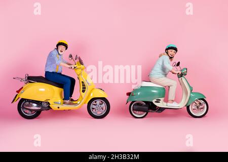Foto in voller Größe von zwei glücklich reifen Menschen männlich weiblich in Helm Reiten Moped extreme fahren isoliert auf rosa Hintergrund Stockfoto
