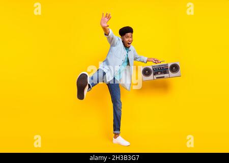 Foto von süß aufgeregt dunkle Haut Kerl gekleidet Denim Hemd gehen singen hören Boom Box isoliert gelbe Farbe Hintergrund Stockfoto