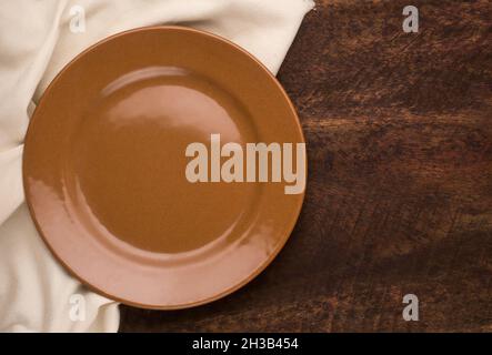Leerer Teller und eine Stoffserviette auf einem Holzhintergrund, Draufsicht mit Kopierplatz für Food-Fotografie Stockfoto