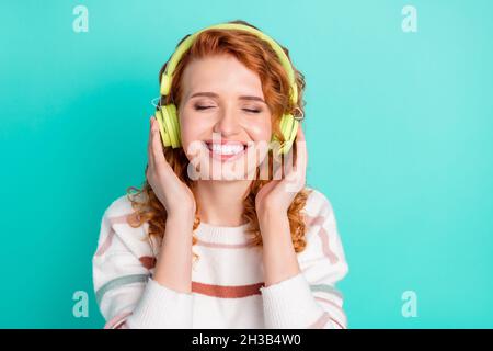 Foto von süßen roten welligen Frisur junge Dame Musik hören tragen Kopfhörer weißen Pullover auf blauem Hintergrund isoliert Stockfoto