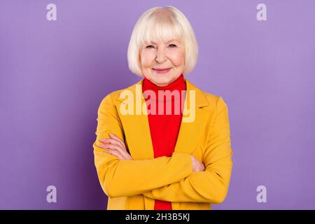 Foto von fröhlichen ziemlich kurze Frisur im Alter Dame gekreuzte Arme tragen gelbe Jacke auf lila Hintergrund isoliert Stockfoto