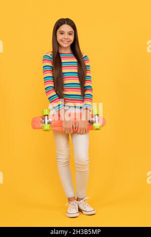 Skateboarding. Fröhliches Kind hält Penny Board. Teen Mädchen auf gelbem Hintergrund. Stockfoto