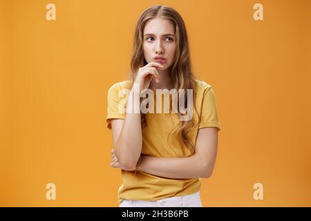 Porträt einer besorgten smarten Frau mit welligem, fadem Haar in legerem T-Shirt, die Hand am Kinn hält und die Lippen schnurrt und mit nachdenklichen Sorgen richtig aussieht Stockfoto