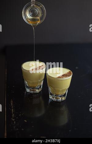 Zwei elegante Gläser mit goldener Milch in gibraltar-Gläsern mit Zimt, während der Barista Zimt darüber tröpfelt. Stockfoto