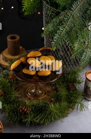Stillleben im Winter. Hausgemachte Muffins, süßes Gebäck auf dem Tisch. Schokoladen-Muffins in einer Glasvase auf einem Stiel. Tannenzweige. Süßes Essen, Dessert. Weihnachtsfeier. Maffin. Stockfoto