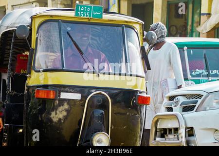 Kahartum, Sudan, ca. 5. Februar 2019: Gelb-schwarz bemalter Tuktuk mit lächelndem Fahrer im Verkehrskreiz der Hauptstadt Stockfoto