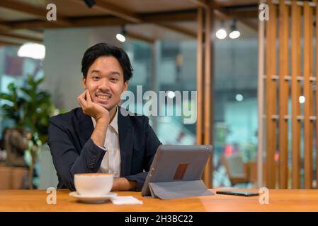 Porträt eines asiatischen Geschäftsmannes, der im Café mit einem digitalen Tablet-Computer sitzt Stockfoto