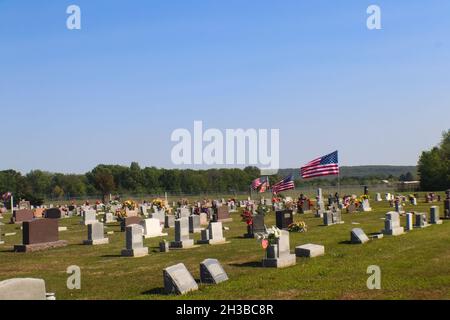 Amerikanische Flaggen, die über dem Friedhof fliegen, geschmückt mit Blumen für den Memorial Day in den Vereinigten Staaten mit Hügeln im Hintergrund Stockfoto