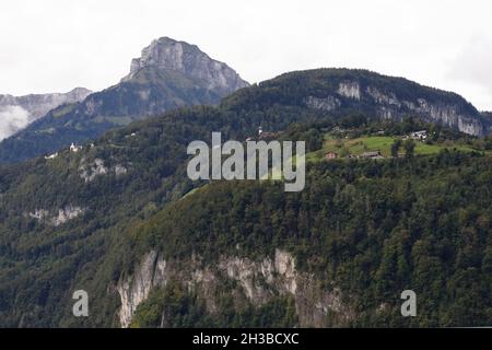 Die alpen, felsige Berge und ihre Hänge sind mit Wäldern bedeckt. Auch Wiesen mit Gebäuden auf ihnen sind vorhanden. Stockfoto