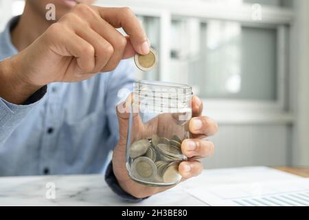 Geschäftsmann Sparen-Konzept. Hand hält Münzen in Krug Glas Stockfoto