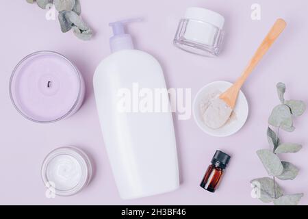 Hautpflege kosmetische Zusammensetzung mit Lotion, Tonpulver, Feuchtigkeitscreme und ätherisches Öl auf lila Hintergrund, flach legen. Stockfoto