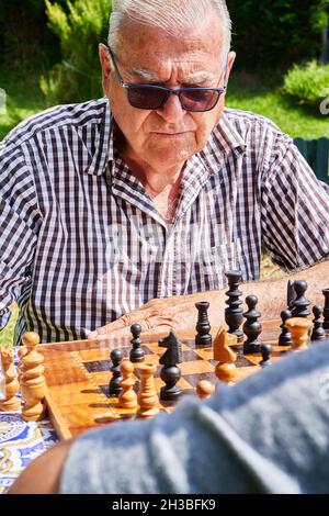 Älterer Mann, der im Garten des Hauses Schach spielt Stockfoto