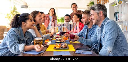 Fröhliche, vielfältige, große Gruppe multikultureller Freunde, die gemeinsam einen salzigen Frühstücksbrunch im Bar-Restaurant im Hotel genießen Stockfoto