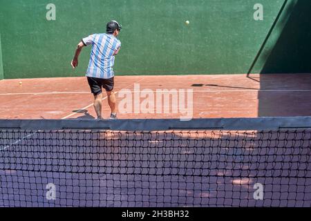 der lateinische Brünette auf dem Rücken spielt alleine Paddle-Tennis, trägt im Urlaub eine Mütze und ein argentinien-T-Shirt.Horizontal Stockfoto