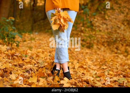 Frauenbeine in Jeans und Stiefeln stehen in gefallenen Blättern. Kopierraum. Geringe Schärfentiefe Stockfoto