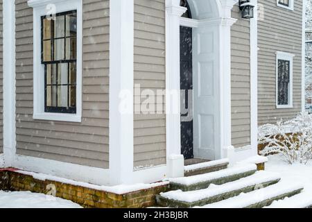 Zwei Vintage-Doppelfenster mit einer schwarzen Tür an einer beigefarbenen Holzaußenwand eines Hauses. Die Fenster sind dunkelgrün mit weißen Zierleisten. Stockfoto
