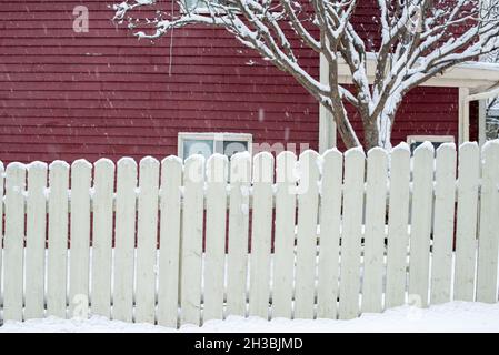 Ein rotes Holzhaus mit einem kleinen Glasfenster. Um das geschlossene Fenster ist ein weißer Rand zu sehen. Im Vordergrund ist ein mit Schnee bedeckter Baum. Stockfoto