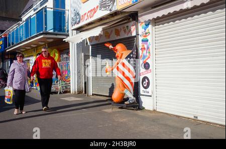 Ein älteres Paar, das in Scarborough am Meer entlang an einem geschlossenen Hot Dog Stand vorbeiläuft. Stockfoto