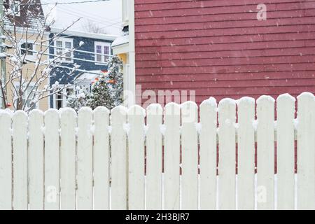 Ein rotes Holzhaus mit einem kleinen Glasfenster. Um das geschlossene Fenster ist ein weißer Rand zu sehen. Im Vordergrund ist ein mit Schnee bedeckter Baum. Stockfoto