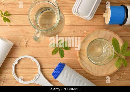 Umkehrosmose-System Wasserreinigungskonzept mit Glas und Krug gefüllt mit gereinigtem Wasser und Filtern und Filtrationsstufen auf Holztisch. Oben Stockfoto