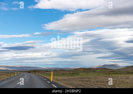 Panoramablick über eine kurvige zweispurige Straße auf Island, durch das karge isländische Hochland mit Vulkanen und Bergen auf der Insel Stockfoto