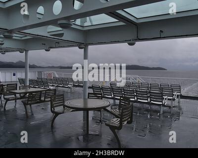 Leere Sitzplätze auf dem hinteren Deck des Fährschiffs, das die kanadische Küste über die Inside Passage passiert, an bewölktem Tag in der Herbstsaison. Stockfoto