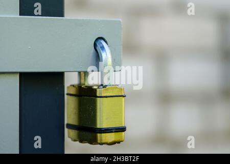 Ein geschlossenes und verriegeltes Messing-Vorhängeschloss hängt in der Türschlaufe auf einem verschwommenen Hintergrund Stockfoto