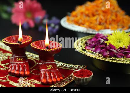 Tonlampe bekannt als Diya, Deep, Diyo, Deepa oder Deepam mit Götterfüßen Lakshmi Charan beleuchtet auf rotem Tuch Asan mit Roli Sindoor Blumen und Bok Stockfoto