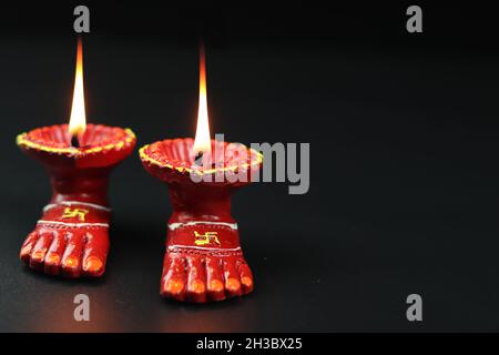 Tonlampe bekannt als Diya, Deep, Diyo, Deepa oder Deepam mit Göttin Füße Lakshmi Charan Beleuchtung in dunkelschwarzem Hintergrund mit Copy Space for Text. Stockfoto