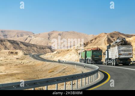 Lastwagen fahren auf der Autobahn zu den felsigen Bergen in der Negev-Wüste. Straße mit Schienen. Stockfoto