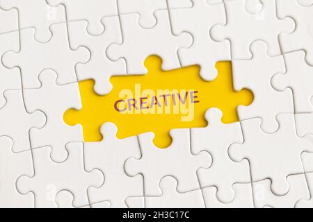 Weiße Details des Puzzles mit dem Text „Creative“ auf gelbem Hintergrund. Stockfoto