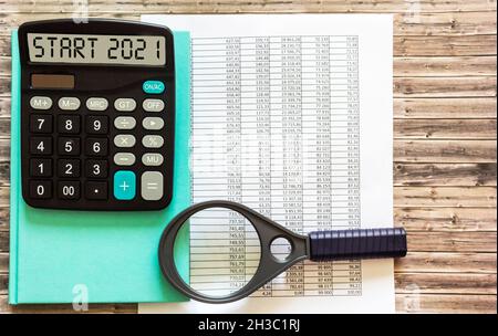 Der Start 2021 wird auf dem Display des Rechners, auf dem Desktop mit Finanzdokumenten und einer Lupe geschrieben. Geschäftskonzept. Stockfoto
