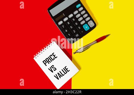 Notizblock mit den Worten Preis vs. Wert, auf rotem und gelbem Hintergrund, neben einem Rechner und einem Stift Stockfoto