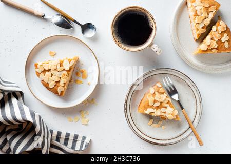 Mandelkuchen und Tasse schwarzen Kaffee. Tortenscheiben mit Mandelflocken auf Dessertplatte, Tischansicht von oben. Graue Betonhintergrundstruktur. Stockfoto