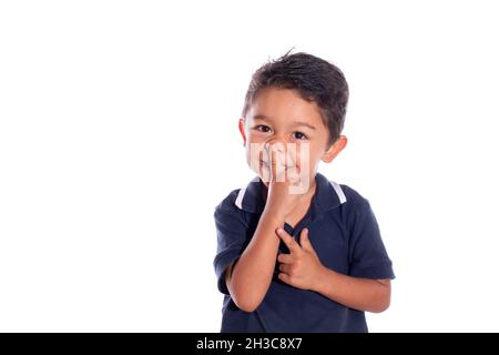 Peinlicher Junge, der versucht, seine Nase zu pflücken, isoliert auf weißem Hintergrund. Lateinisches Kind lacht, während es seine Nasenspitze berührt. Stockfoto