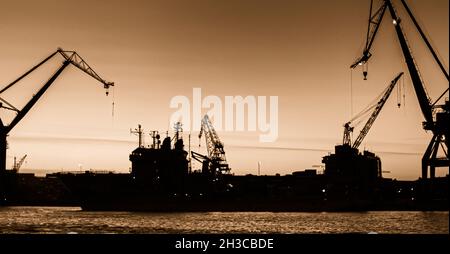 Silhouetten von Schiffen und Kränen an einem Kai Stockfoto