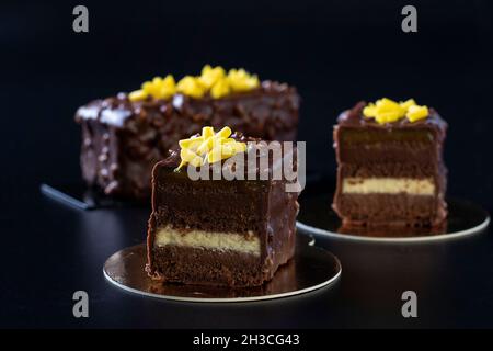 Schokoladenmandel-Brownie mit Mango- und Passionsfrucht-Marmelade überzogen Gourmet-Schokoladenglasur auf schwarzem Hintergrund. Nahaufnahme Stockfoto