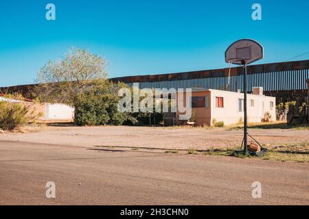Ein Basketballkorb auf der Straße in der US-Grenzstadt Naco, Arizona. Dahinter ragt die hohe, verrostete Stahlgrenzmauer zwischen den USA und Mexiko Stockfoto