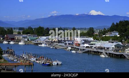 REGENBOGENBRÜCKE BLICK AUF DAS MALERISCHE DORF LA CONNER, WASHINGTON UND DEN SWINOMISH CHANN ... MIT MT BAKER UND DEN WASHINGTON KASKADEN IN DER FERNE. Stockfoto