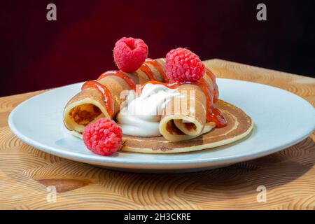 Helsinki / Finnland - 27. OKTOBER 2021: Eine Platte mit flauschigen norwegischen Pfannkuchen mit karamellisierter Schlagsahne und Himbeermarmelade auf der Seite. Stockfoto