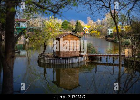 Holzschuppen mit einer kleinen Brücke auf einem See, eingerahmt von Baumzweigen; Geheime Orte in Ungarn Tapete Stockfoto